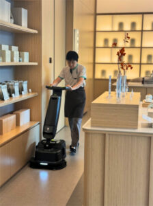 A spa staff member operates a PUDU robotic floor cleaner in a modern wellness center, ensuring spotless floors with automation.