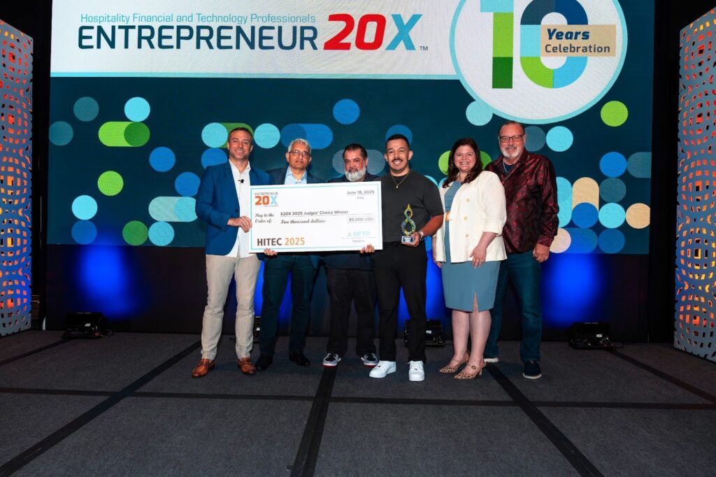 A group of six people standing on stage at HITEC 2025, holding a large cheque and trophy for the Entrepreneur 20X Judges' Choice Winner.
