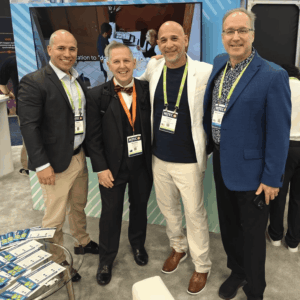 Four men smiling and posing together at a HITEC 2025 event booth.